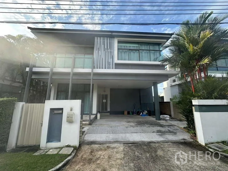 Detached House for rent or sale in Bang Kapi, Bangkok - Modern two-storey detached house with large windows, palm trees and a covered double carport at the front.