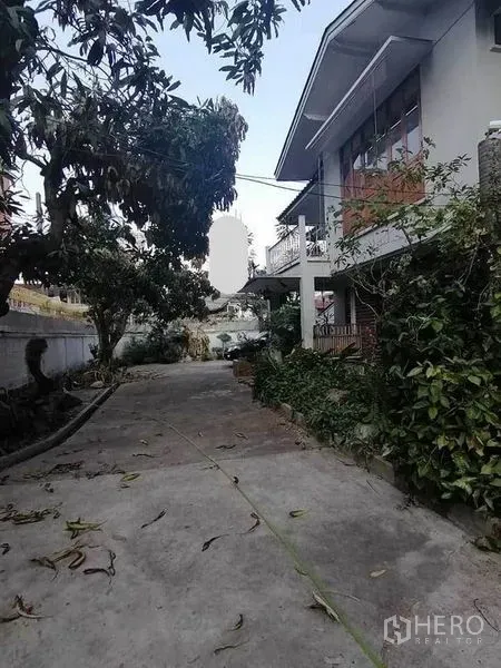Detached House for rent in Pathum Wan, Bangkok - Exterior driveway and garden with mature trees beside a two-storey house.