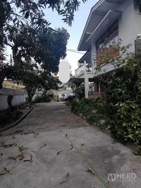 Detached House for rent in Pathum Wan, Bangkok - Exterior driveway and garden with mature trees beside a two-storey house.
