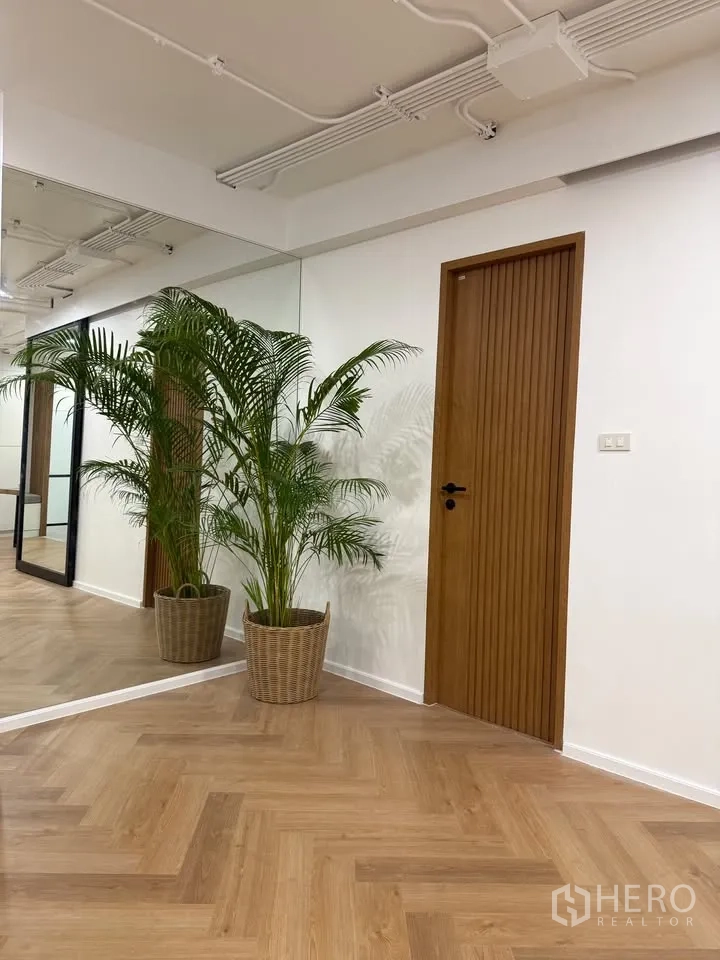 Condominium for rent in Watthana, Bangkok - Hallway with mirrors, wood doors, and potted palms on herringbone floor.