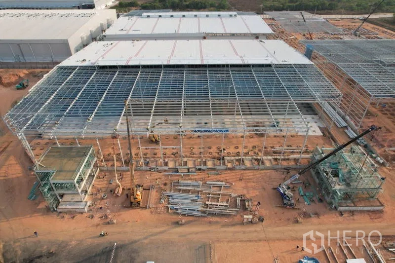 Factory for rent in Bang Bo, Samut Prakan - Front aerial of an expansive warehouse steel structure with cranes, stacked materials, and two attached service buildings.