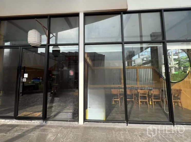 พื้นที่ขายปลีก ให้เช่าในWatthana, Bangkok - หน้าร้านกระจกสูง มองเห็นที่นั่งภายในและโคมแขวนเหนือทางเท้า.