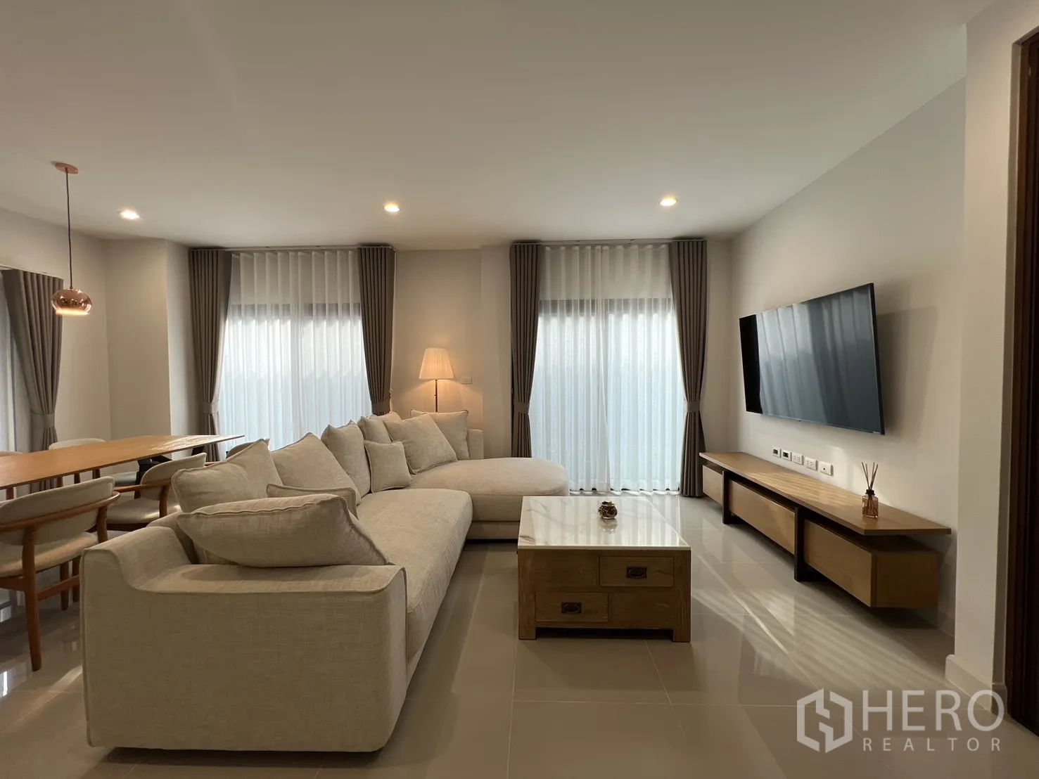 Detached House for rent in Prawet, Bangkok - Living area with wall-mounted TV, sofa and sheer curtains.