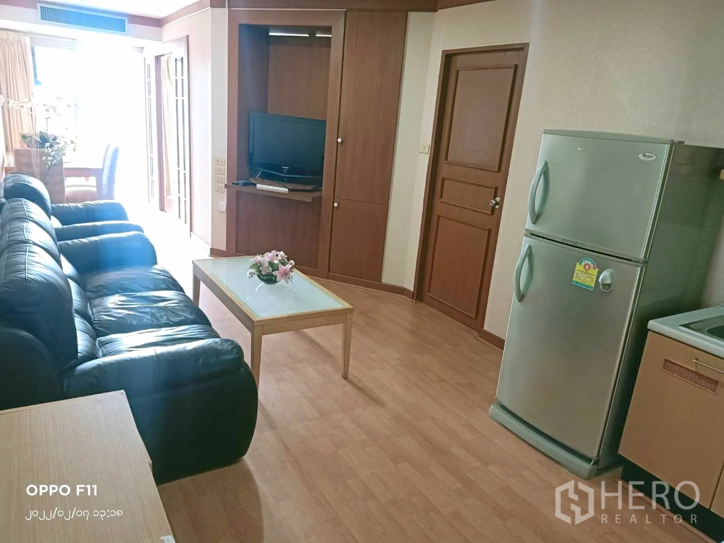 คอนโด ให้เช่าในKhlong Toei, Bangkok - พื้นที่นั่งเล่นสว่างพร้อมโซฟา โต๊ะกลาง และครัวมีตู้เย็นสีเงิน