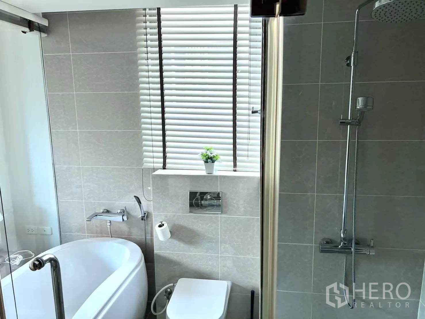 คอนโด ขายในWatthana, Bangkok - ห้องน้ำในตัวมีอ่างอาบน้ำ โถสุขภัณฑ์แขวนผนัง และเรนชาวเวอร์ข้างหน้าต่างบานเกล็ด