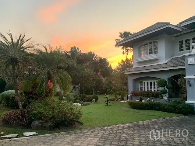 独立式住宅 出租在Khan Na Yao, Bangkok - 日落中的景观花园，棕榈树、修剪草坪与石径，紧邻房屋。