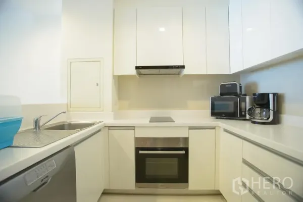 Apartment for rent in Khlong Toei, Bangkok - Bright U-shaped white kitchen with built-in oven, cooktop, dishwasher and ample cabinetry in a Phrom Phong apartment.