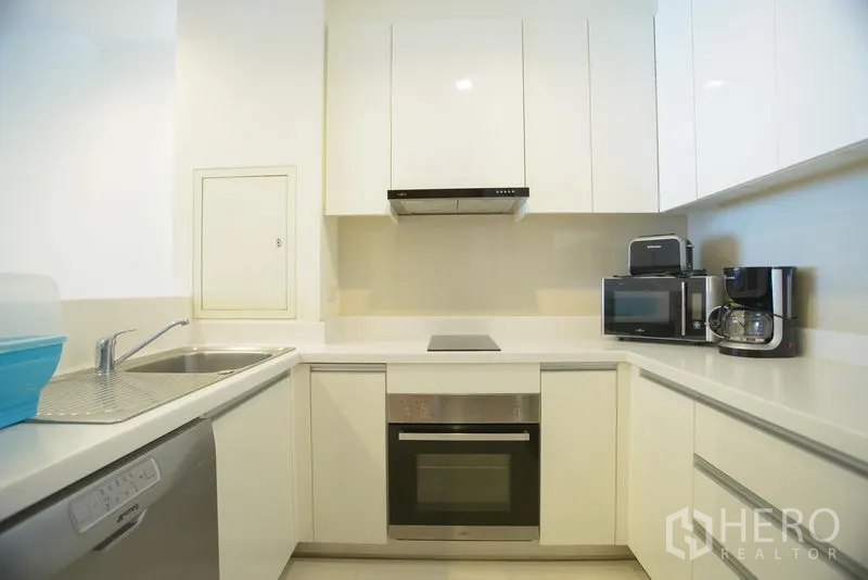 Apartment for rent in Khlong Toei, Bangkok - Bright U-shaped white kitchen with built-in oven, cooktop, dishwasher and ample cabinetry in a Phrom Phong apartment.