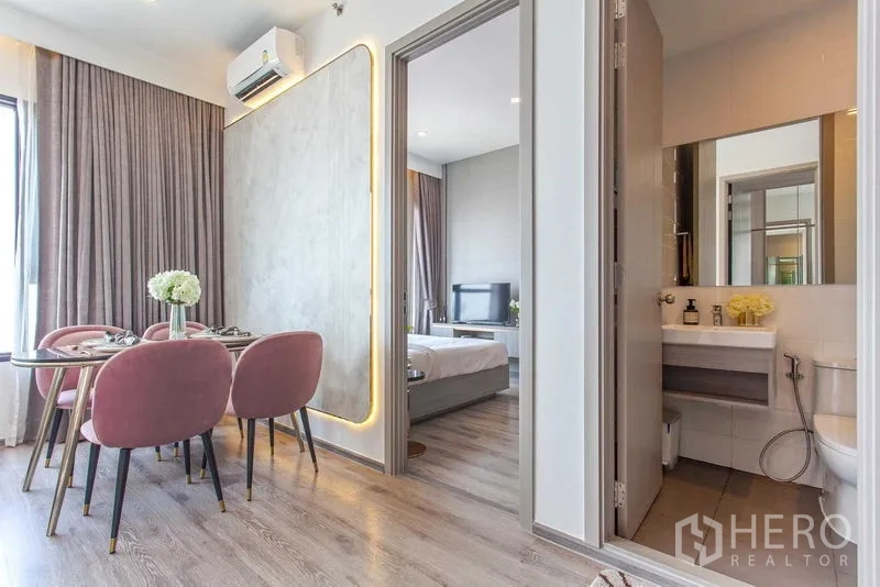 Condominium for rent in Watthana, Bangkok - Dining nook with pink upholstered chairs next to a feature wall, doors leading to a bedroom and bathroom.