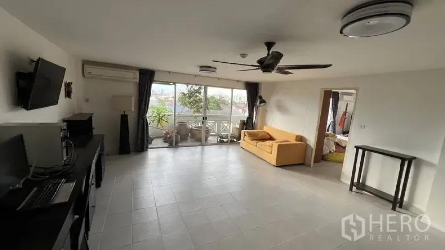 Condominium for sale in Wang Thonglang, Bangkok - Bright tiled living room with ceiling fan opening to a deep balcony with greenery in a Wang Thonglang condo.