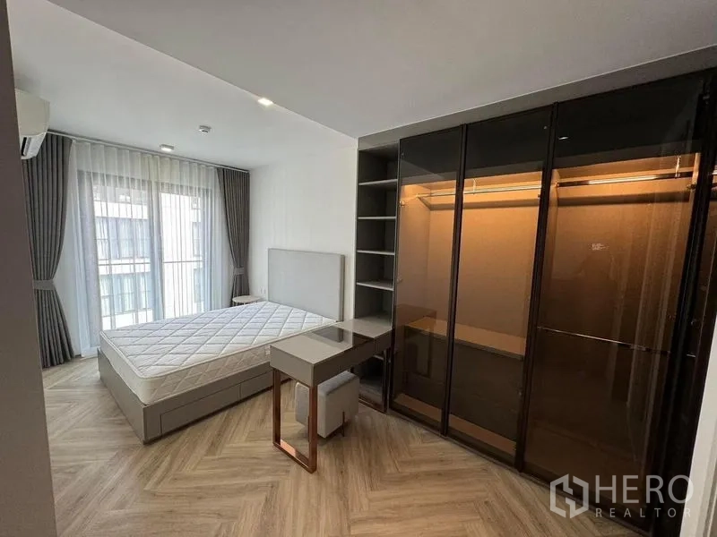 Condominium for rent in Watthana, Bangkok - Bedroom featuring a glass-door wardrobe, study desk and large curtained windows.