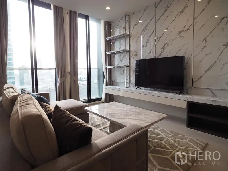 Condominium for rent in Pathum Wan, Bangkok - Living room with marble feature wall, large TV, sectional sofa and floor-to-ceiling windows.