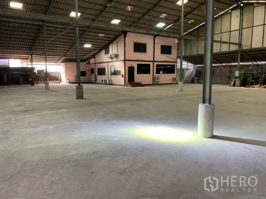 Warehouse for rent - Open floor area with task lights and a fire extinguisher near steel columns.