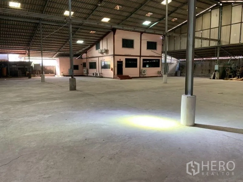 Warehouse for rent - Open floor area with task lights and a fire extinguisher near steel columns.
