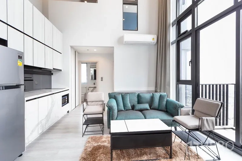 Condominium for rent in Phra Khanong, Bangkok - Open-plan living area with marble-look kitchen, teal sofa and expansive windows.