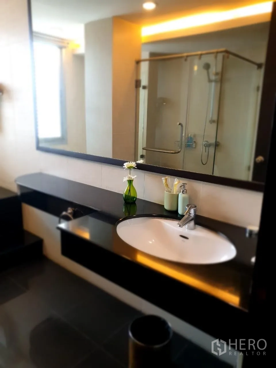 Apartment for rent in Bang Rak, Bangkok - Contemporary bathroom vanity with large mirror and glass-enclosed shower.