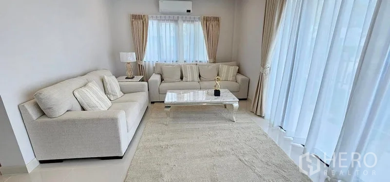 Detached House for rent in Bang Phli, Samut Prakan - Bright living room with two cream sofas, a marble coffee table and floor-to-ceiling curtains.