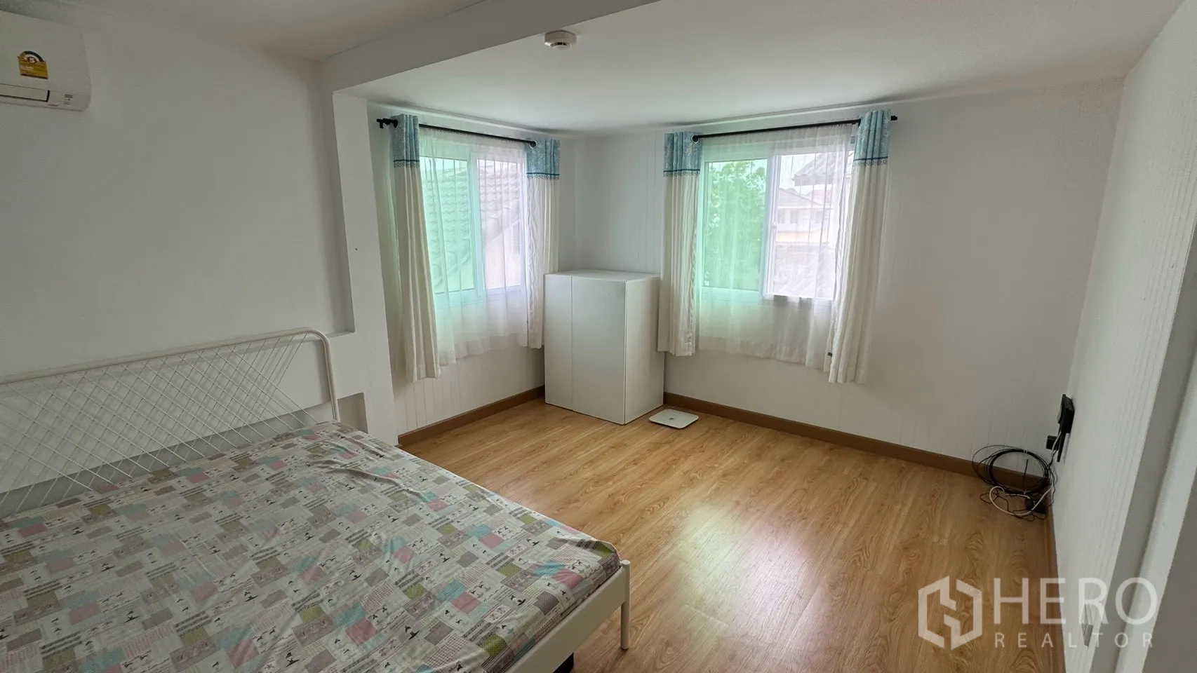 Detached House for rent in Saphan Sung, Bangkok - Spacious bedroom with three windows, wood floors, and a small cabinet.