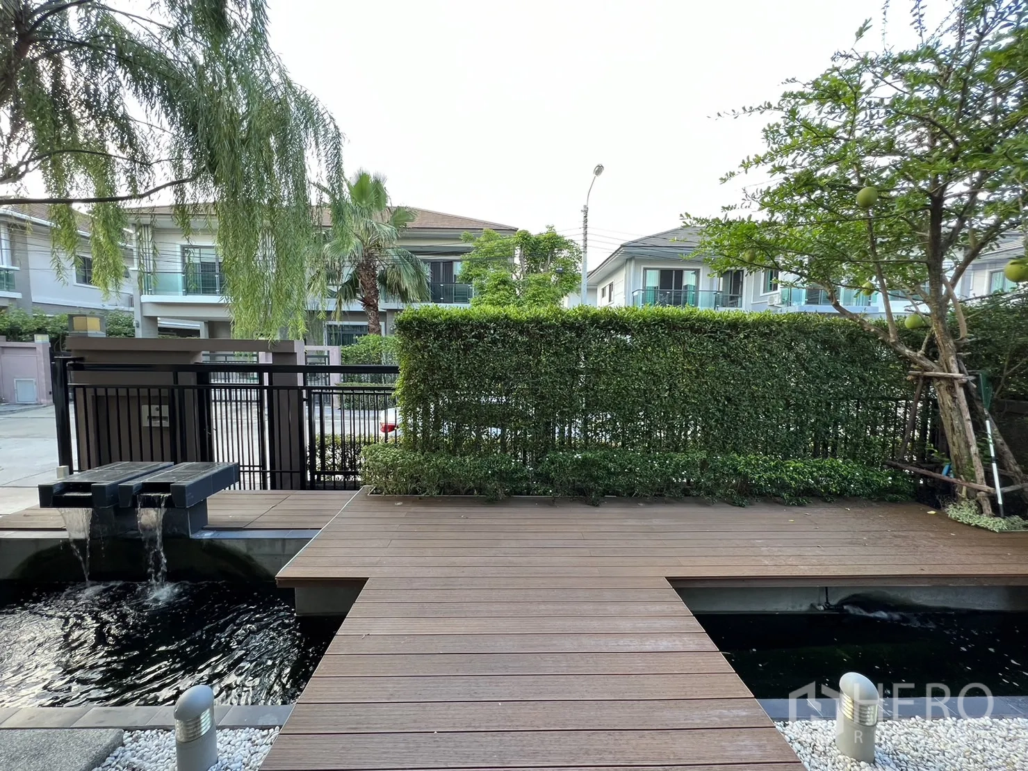 Detached House for rent in Suan Luang, Bangkok - Front yard deck with decorative water feature and street view beyond hedge fence.