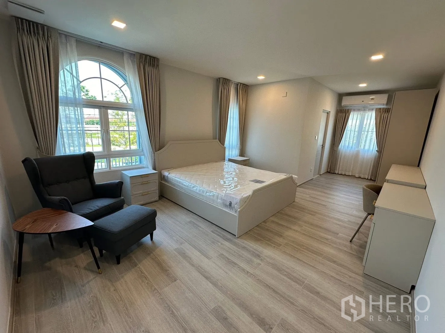 Detached House for rent in Bang Phli, Samut Prakan - Large master bedroom with arched window, lounge chair, and desk.