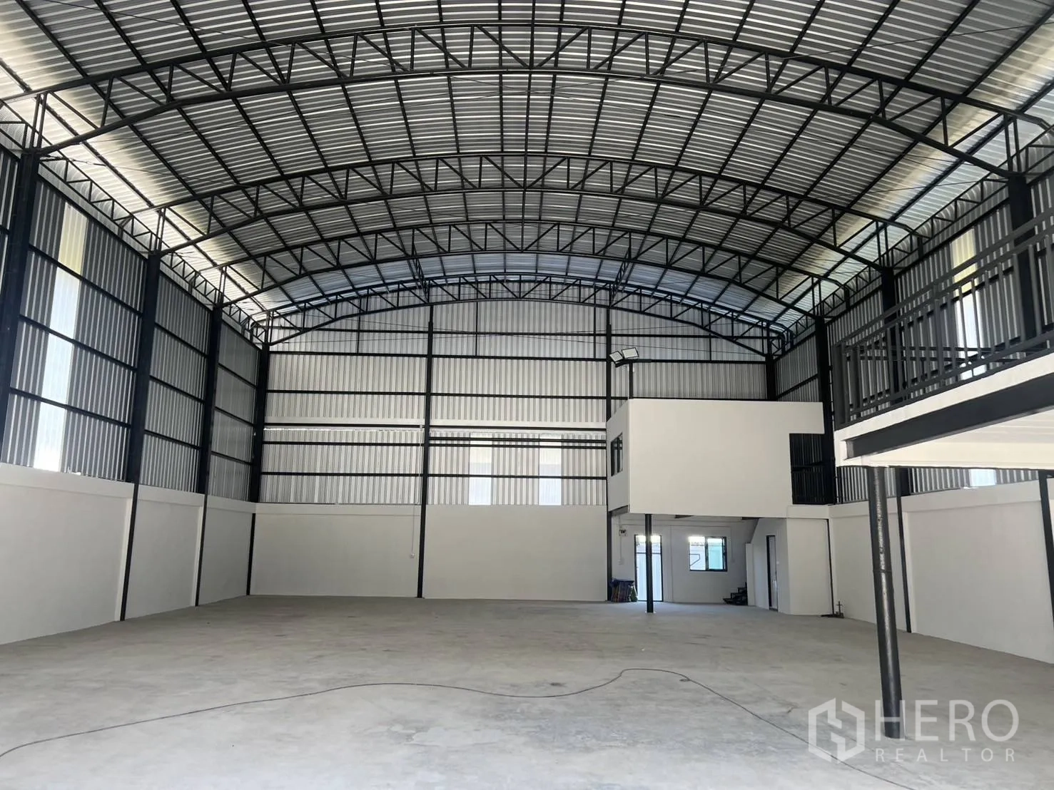Warehouse for rent in Bang Phli, Samut Prakan - Interior of steel-frame warehouse with high arched roof, open concrete floor, and mezzanine office block.