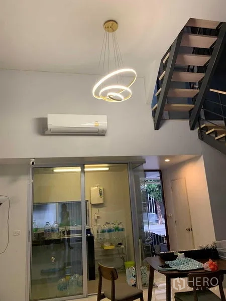 联排别墅 出租在Khan Na Yao, Bangkok - 餐区配现代环形吊灯，楼梯与玻璃推拉门厨房。