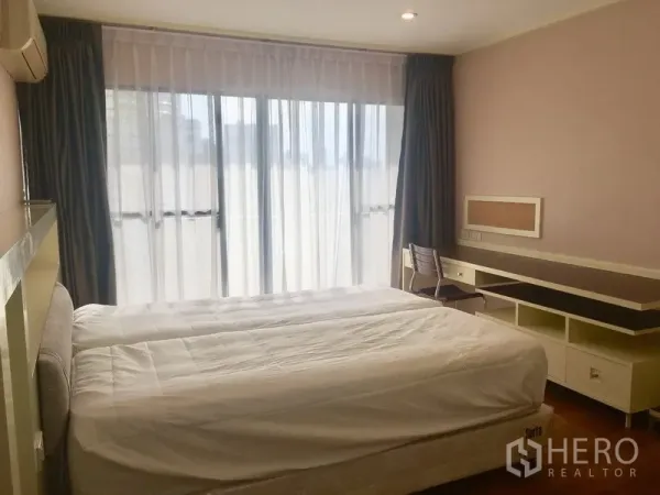 Condominium for rent in Watthana, Bangkok - Primary bedroom with king bed, sheer curtains, work desk and access to the balcony.