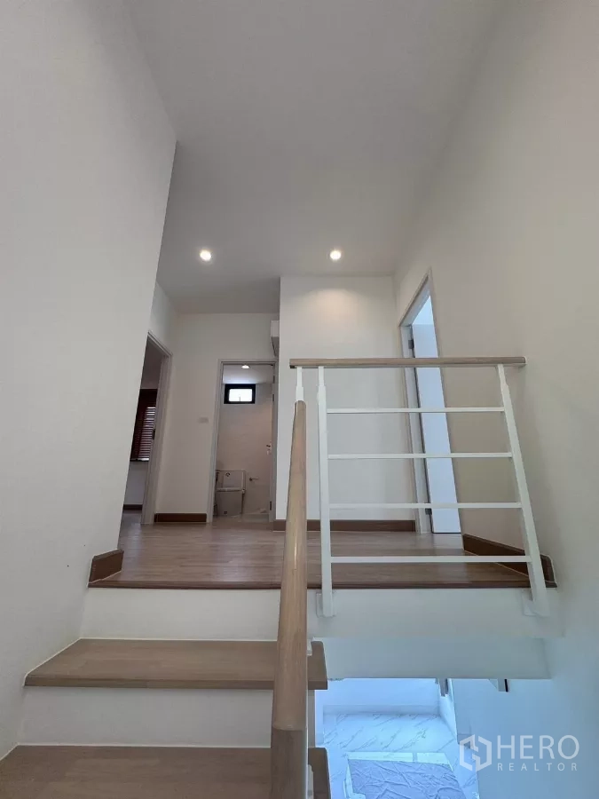 Detached House for rent in Samut Prakan - Upper landing with wooden staircase and white railing.