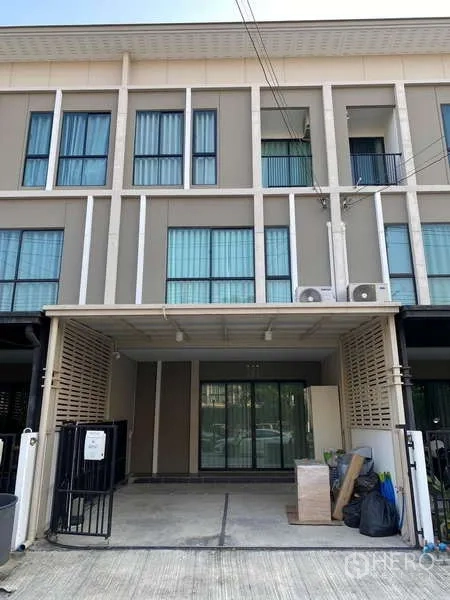 Townhouse for rent in Bang Kapi, Bangkok - Modern three-storey townhouse facade with blue-tinted windows and gated carport.