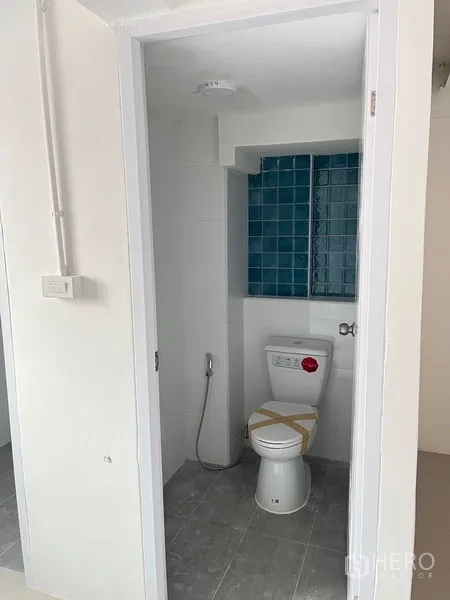 พื้นที่ขายปลีก ให้เช่า - ห้องน้ำขนาดกะทัดรัดพร้อมโถสุขภัณฑ์ สายฉีดชำระ และผนังกระเบื้องสีน้ำเงิน