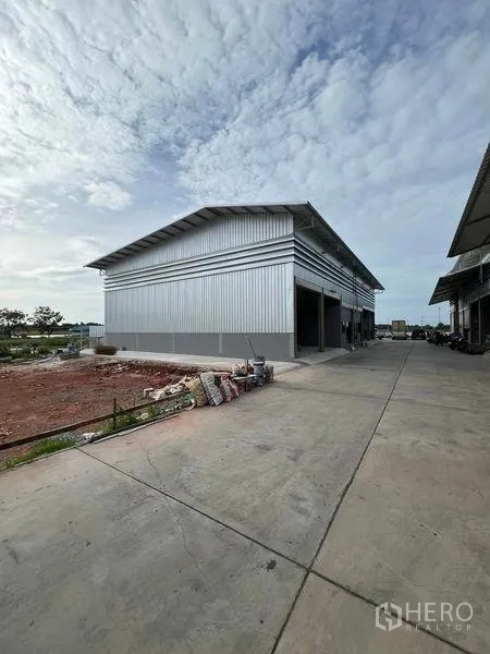 Warehouse for rent in Phra Samut Chedi, Samut Prakan - Corner view of the new metal-clad warehouse beside a wide concrete driveway.
