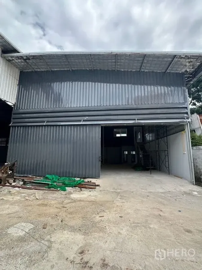 Warehouse for rent in Suan Luang, Bangkok - Front facade of a grey metal warehouse with open loading bay and driveway suitable for trucks.
