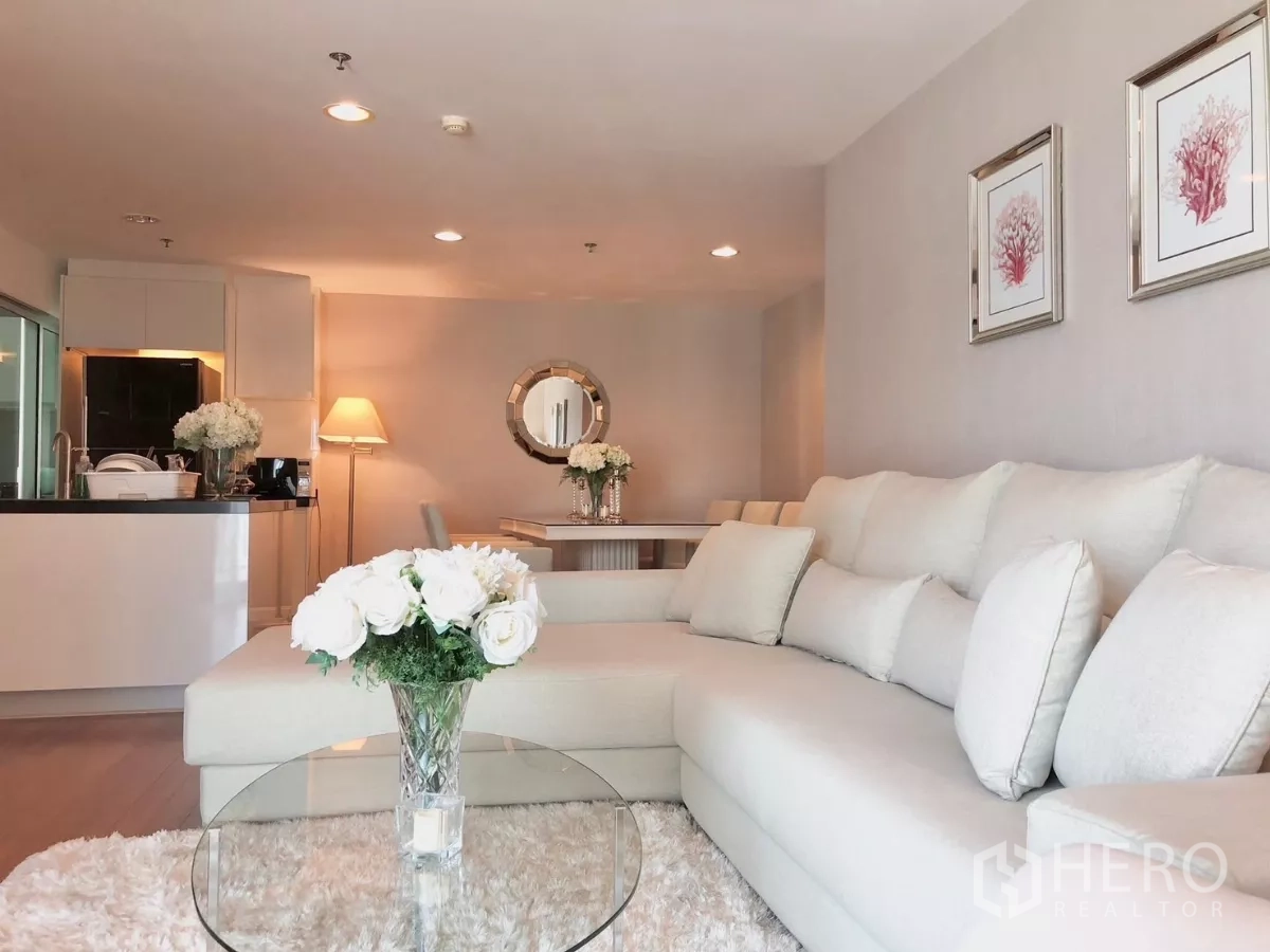 Condominium for rent in Huai Khwang, Bangkok - Spacious living and dining area with sectional sofa, plush rug and modern kitchenette on a high floor.