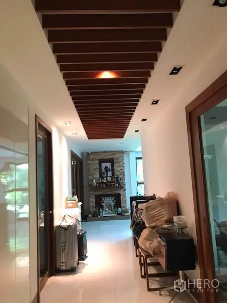 独立式住宅 出售在Lat Phrao, Bangkok - 明亮走廊，木格栅天花、筒灯与通往各房的玻璃门。