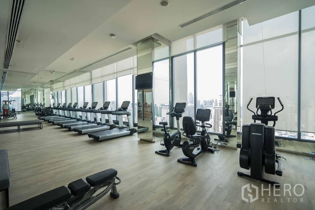 Condominium for rent in Watthana, Bangkok - Large fitness center with treadmills, bikes and city views through tall windows.