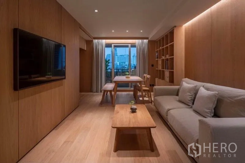 คอนโด ให้เช่าในPhaya Thai, Bangkok - ห้องนั่งเล่นโทนไม้ อบอุ่น พร้อมโซฟา ทีวี โต๊ะทานอาหาร และระเบียงชมวิวเมืองยามค่ำ