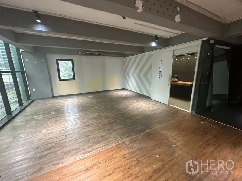 办公空间 出租在Bang Rak, Bangkok - 角落工作区，木地板，箭头纹理装饰墙，滑门通向玻璃会议室。