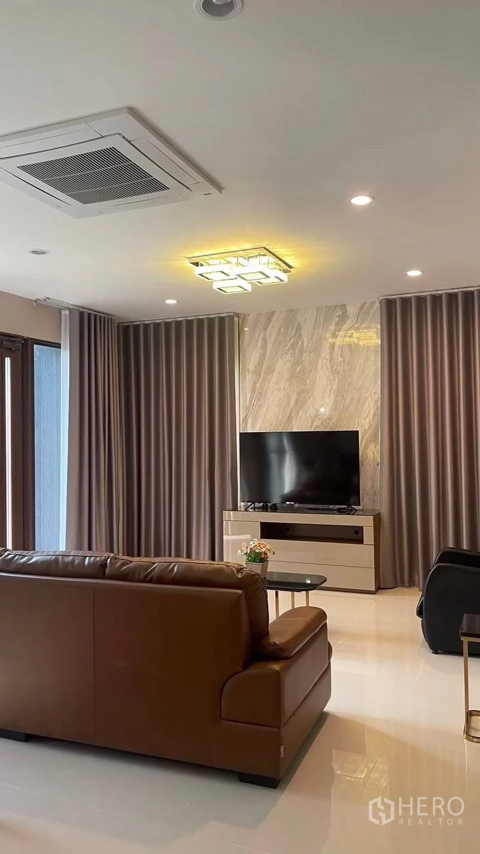 Detached House for rent in Prawet, Bangkok - Spacious living area with TV on marble accent wall and ceiling cassette air conditioner.