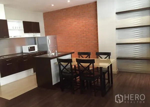 อพาร์ทเมนท์ ให้เช่าในKhlong Toei, Bangkok - ครัวแบบเปิดพร้อมเคาน์เตอร์ซิงก์ ตู้ลายไม้สีเข้ม ผนังอิฐ และโต๊ะทานอาหาร 4 ที่ ในอพาร์ตเมนต์ย่านวัฒนา กรุงเทพฯ