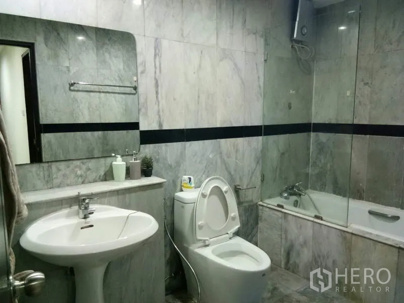 Condominium for rent in Watthana, Bangkok - Marble-tiled bathroom with bathtub and glass shower screen, vanity and toilet.