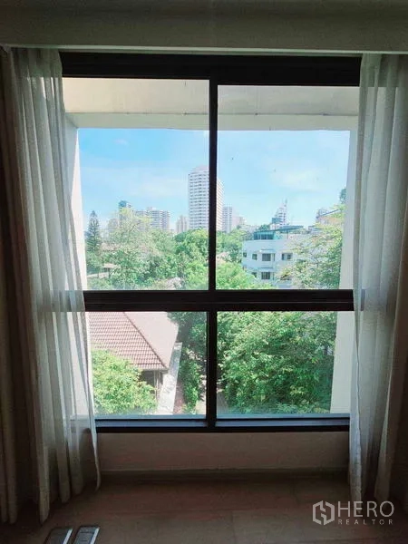 Condominium for rent - Window view across leafy low-rise homes to Bangkok high-rises.