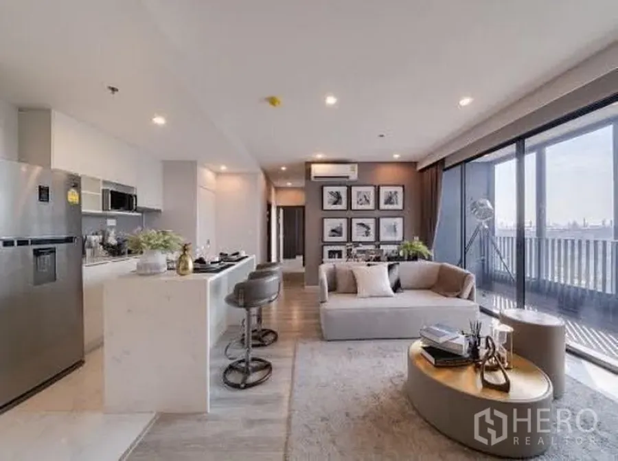 公寓 出租在Bang Na, Bangkok - 沙发与厨房面对整面落地玻璃，连接阳台，远眺城市景观。