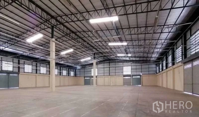Warehouse for rent in Bang Bo, Samut Prakan - Empty warehouse bay showing multiple roller shutter doors and ventilated louvered windows.
