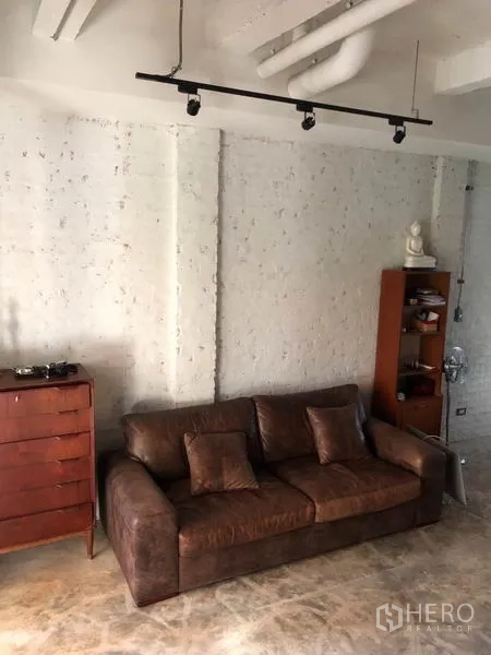 ทาวน์เฮาส์ ขายในWang Thonglang, Bangkok - มุมนั่งเล่นอบอุ่นด้วยโซฟาหนังสีน้ำตาล ผนังอิฐฉาบสีขาว และรางไฟส่องสว่าง