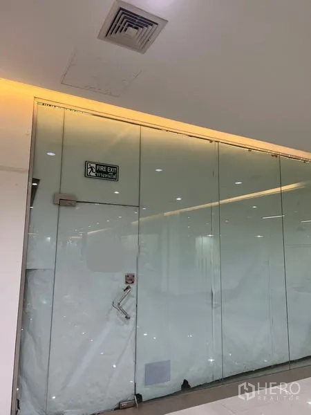 พื้นที่ขายปลีก ให้เช่า - หน้าร้านกระจกเต็มบานพร้อมป้ายทางหนีไฟและไฟฝังฝ้า บริเวณโถงศูนย์การค้าในเขตวัฒนา กรุงเทพฯ