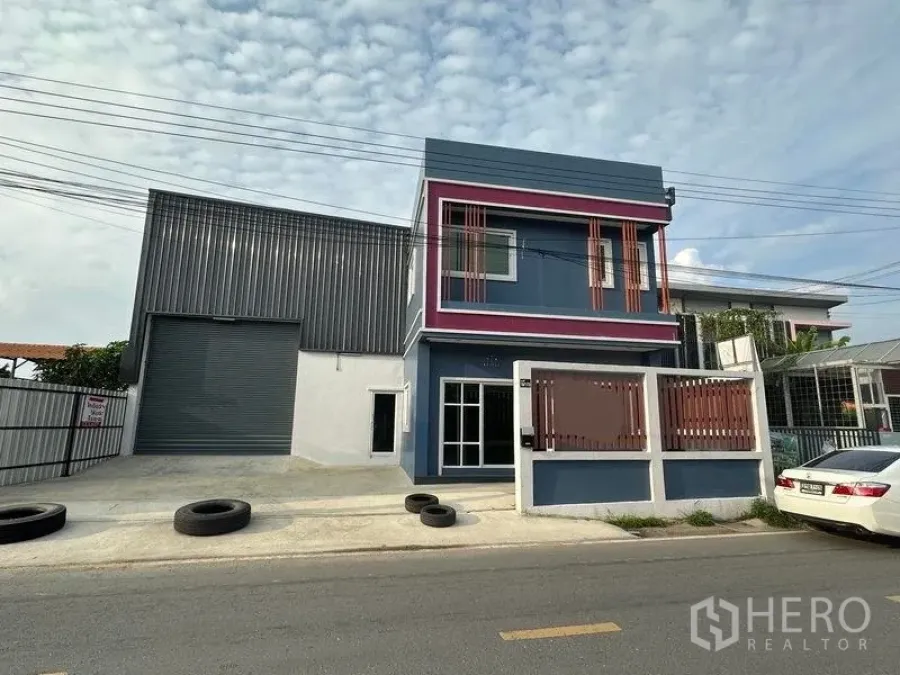 货栈 出租在Lam Luk Ka, Pathum Thani - 临街仓库外观，带大型卷帘门与两层蓝色办公区，前方有大门与停车位