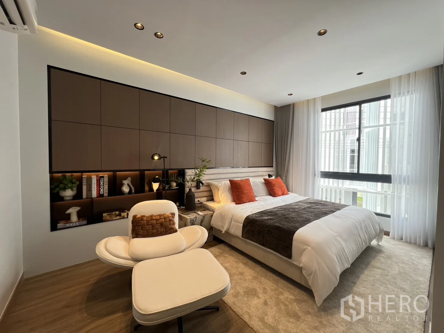 Townhouse for rent in Mueang Samut Prakan, Samut Prakan - Spacious master bedroom with large windows, feature wall cabinetry, and lounge chair.