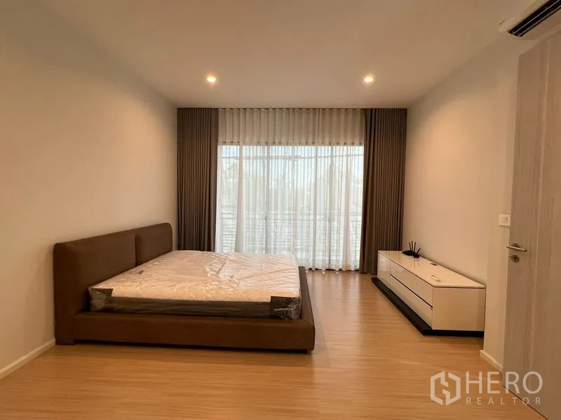 Townhouse for rent in Suan Luang, Bangkok - Spacious master bedroom with a bed, TV console and full-height windows with sheer curtains.