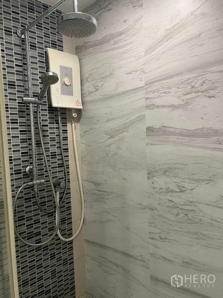 公寓 出售在Bang Na, Bangkok - 淋浴区，雨淋花洒与即热式热水器，灰色瓷砖墙面。
