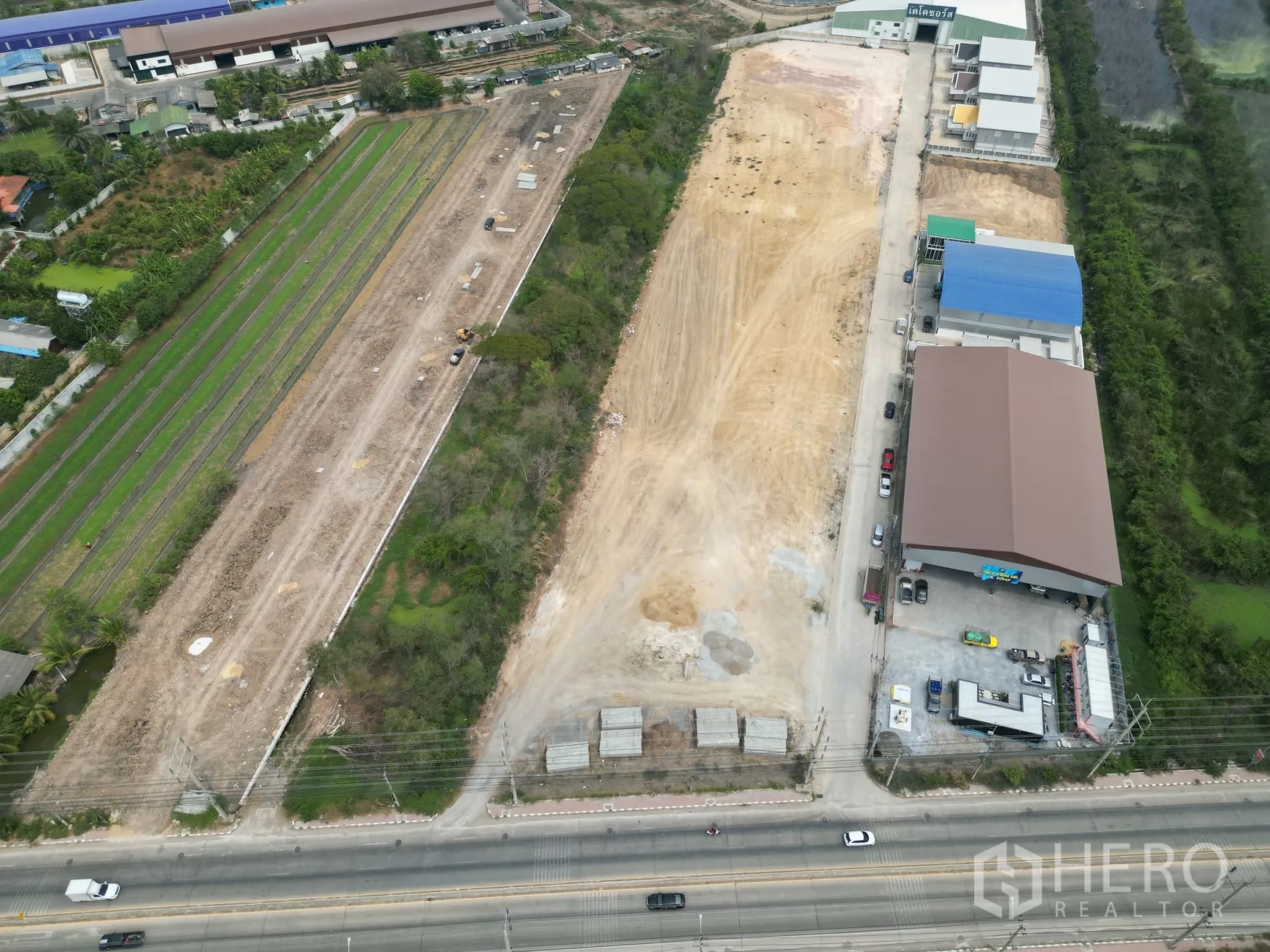 Land for sale in Sai Noi, Nonthaburi - Drone shot showing the land beside a main road, neighboring warehouses, and surrounding fields.